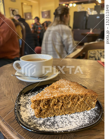 slice of cake and cup of coffee or tea on table over blurred people in cafe 132311849