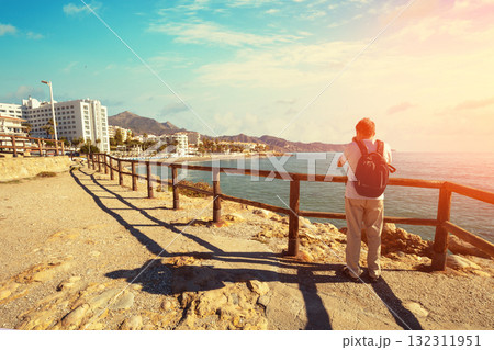 A tourist takes pictures of the Malaga promenade and Torrecilla beach from Torrecilla Viewpoint, Nerja, Malaga, Spain 132311951