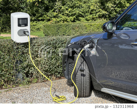 Electric car charging at outdoor station with yellow cable in eco-friendly park slot Electric car charging at outdoor station with yellow cable in eco-friendly park slot 132311968