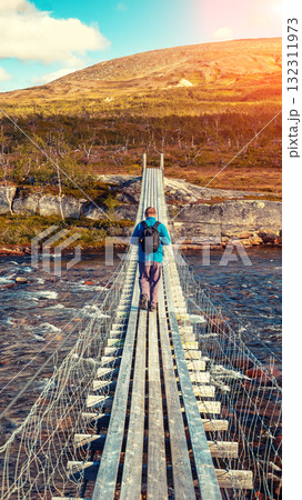 A man crosses a mountain river on a suspension bridge. Vertical banner A man crosses a mountain river on a suspension bridge. Vertical banner 132311973