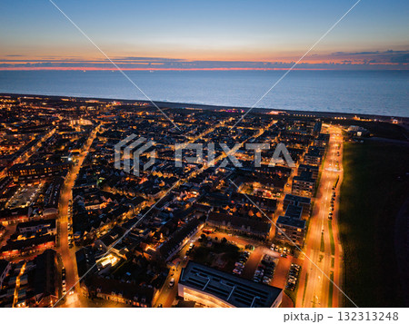 Aerial dusk view of coastal city streetlights and building lights glow against darkening sky, ocean meets horizon, structured grid of streets blends with natural sunset beauty. Aerial dusk view of coastal city streetlights and building lights glow against darkening sky, ocean meets horizon, structured grid of streets blends with natural sunset beauty. 132313248