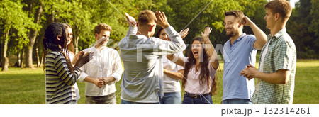 Group of happy young people having fun giving each other high five walking in summer park. 132314261