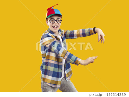 Happy funny child in shirt, propeller cap and glasses dancing on orange background 132314289