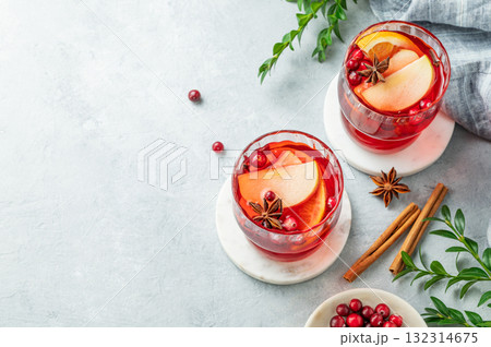 A cranberry drink in a two glasses on a light background with cinnamon, berries and green branch. A cranberry drink in a two glasses on a light background with cinnamon, berries and green branch. 132314675
