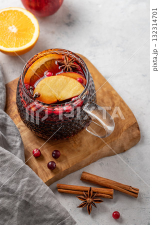 A cup of red mulled wine with spices, orange and apple slices on a wooden board on  light background 132314701