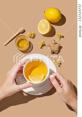 Hand holding cup of hot tea with lemon, ginger and honey on a beige background Hand holding cup of hot tea with lemon, ginger and honey on a beige background 132314737