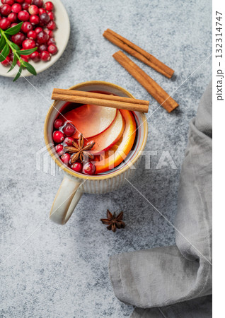 A hot cranberry Christmas drink in a mug on a gray background with cinnamon, berries and napkin. A hot cranberry Christmas drink in a mug on a gray background with cinnamon, berries and napkin. 132314747
