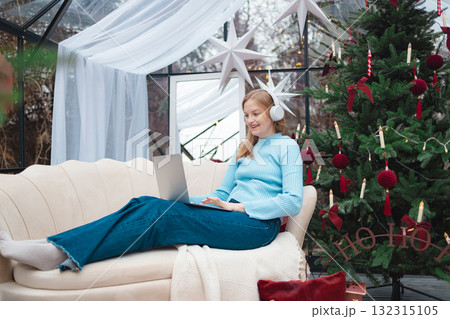 Smiling blonde Caucasian woman working on laptop near Christmas tree Smiling blonde Caucasian woman working on laptop near Christmas tree 132315105