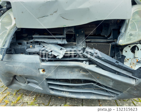 Damaged car front after an accident on a city street captured in the daylight showing broken pieces and a bent structure needing repair 132315623