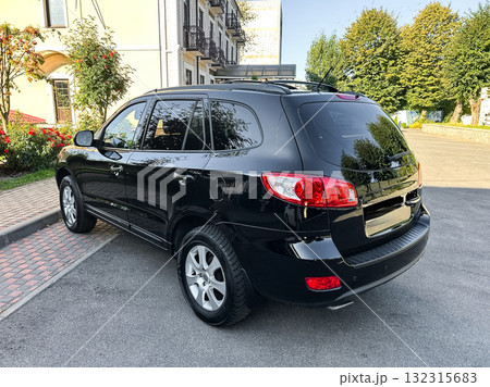 Sleek black SUV parked near a modern building with lush greenery under a clear blue sky in a quiet neighborhood setting 132315683