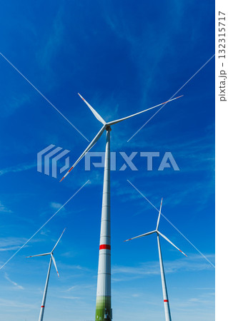 Giant wind turbines stand tall against a bright blue sky in a renewable energy landscape at mid-afternoon Giant wind turbines stand tall against a bright blue sky in a renewable energy landscape at mid-afternoon 132315717