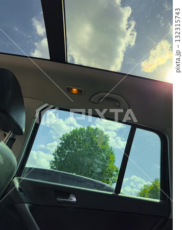Bright afternoon drive with a view of fluffy clouds and green trees from the car's sunroof 132315743