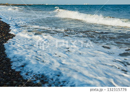 Waves gently crashing on a rocky shore in a serene coastal setting under a clear blue sky during the late afternoon sun 132315776