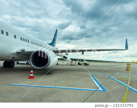 Passengers prepare for departure as a large aircraft stands on the tarmac beneath a dramatic sky filled with clouds 132315795