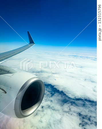 Flying high above the clouds with a view of the airplane wing and powerful engine against a clear blue sky 132315796