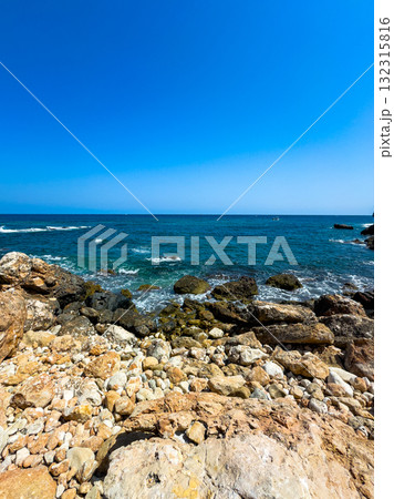 Bright blue ocean waves crash against rocky shores under a clear sky on a peaceful summer day by the sea 132315816
