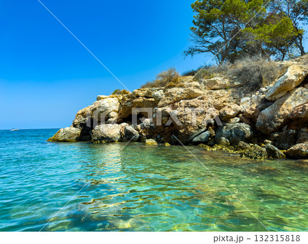 Natural beauty shines in a serene cove with clear turquoise waters and rocky cliffs under a bright blue sky on a sunny day Natural beauty shines in a serene cove with clear turquoise waters and rocky cliffs under a bright blue sky on a sunny day 132315818