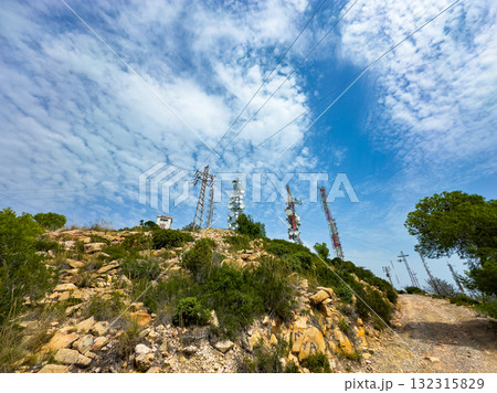 Stunning view of communication towers on a rocky hillside under a bright blue sky with fluffy clouds Stunning view of communication towers on a rocky hillside under a bright blue sky with fluffy clouds 132315829