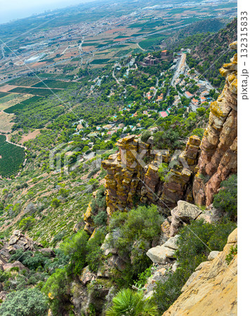 Stunning view of a valley from a rocky cliff with diverse landscape and a distant town during daytime Stunning view of a valley from a rocky cliff with diverse landscape and a distant town during daytime 132315833