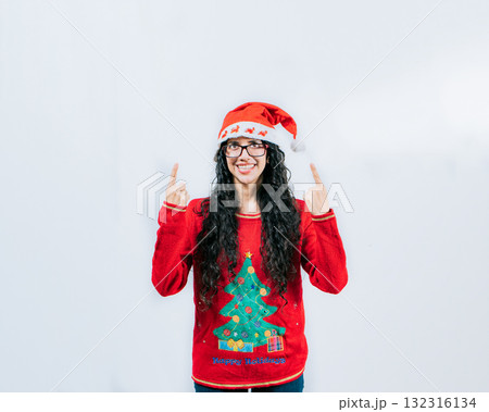 Smiling girl in Christmas hat pointing up isolated. Beautiful girl in Christmas sweater showing and pointing up 132316134