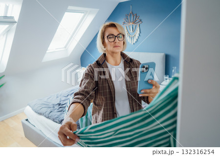 Middle aged Woman taking photo of shirt using smartphone for selling or donating her clothes. Decluttering , Sorting Clothes, And Cleaning Up wardrobe. Reuse, second-hand concept. Conscious consumer. Middle aged Woman taking photo of shirt using smartphone for selling or donating her clothes. Decluttering , Sorting Clothes, And Cleaning Up wardrobe. Reuse, second-hand concept. Conscious consumer. 132316254