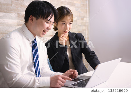オフィスでパソコンを見ながら打ち合わせをする若い男女 132316690