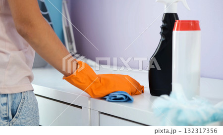 Teen girl with orange gloves cleans her tidy desk with a cloth in organized bedroom Teen girl with orange gloves cleans her tidy desk with a cloth in organized bedroom 132317356