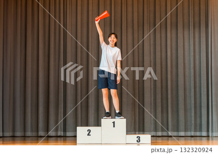 体育館のステージで表彰台に乗る体操着姿の小学生,中学生,高校生の女の子 132320924