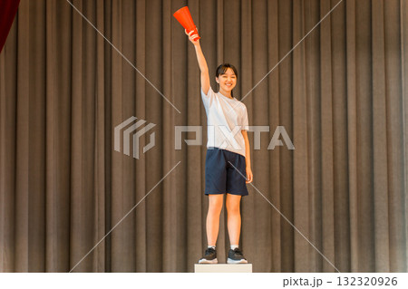 体育館のステージで表彰台に乗る体操着姿の小学生,中学生,高校生の女の子 132320926