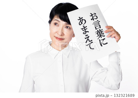 お言葉に甘えてと書かれた紙を片手で持ち視線を送るシニア女性 132321689