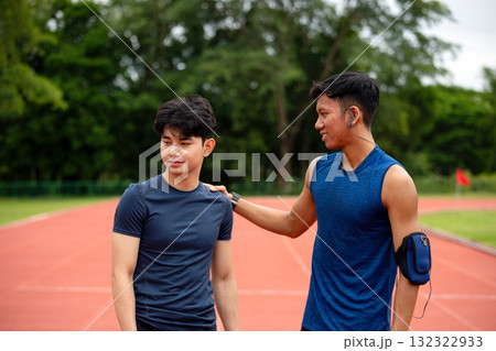 Asian male athlete putting a hand on teammate's shoulder on an outdoor track, symbolizing support, encouragement, friendship, and motivation during sports training or after competition 132322933