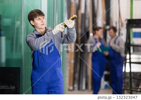 Young guy measures sheet of glass with device Young guy measures sheet of glass with device 132323047