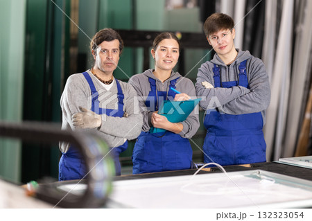 Girl and two male glazier employees with documents speaking and advising in workshop 132323054