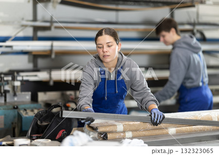 Girl glazer employee in blue overall works in glass processing shop Girl glazer employee in blue overall works in glass processing shop 132323065