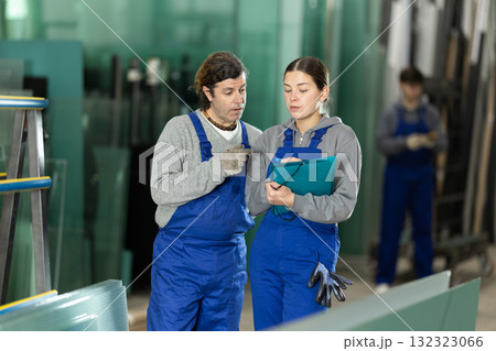 Girl and adult man glazier employees with documents speaking and advising in workshop 132323066