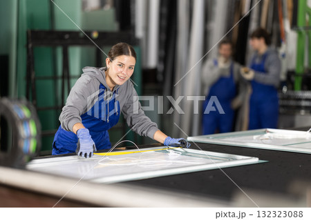 Young woman employee in blue overall measures given length of plastic material 132323088