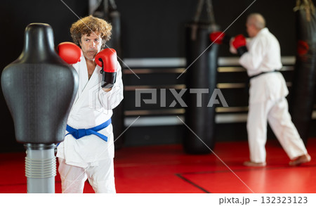 Man in white kimono trains in gym - he punches sports dummy Man in white kimono trains in gym - he punches sports dummy 132323123