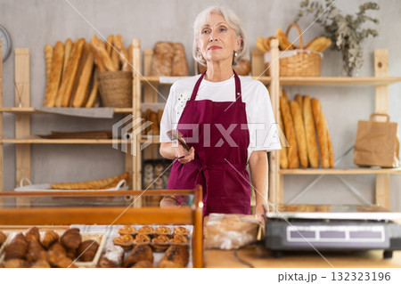 Elderly female seller with tongs in bakery 132323196