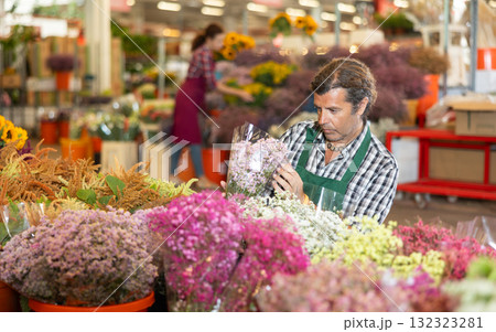 Middle-aged salesman holding bouquet of dry flowers in plants market 132323281