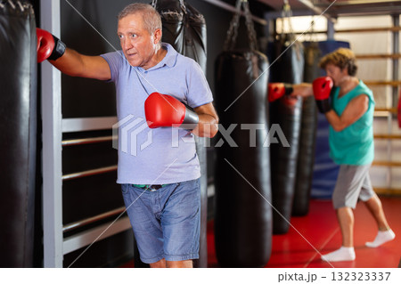 Senior man training punches on heavy bag in gym Senior man training punches on heavy bag in gym 132323337