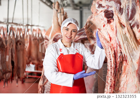 Female butcher in slaughterhouse showing piece of cow carcass 132323355
