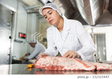 Female butcher preparing raw pork ribs for sale in butchery Female butcher preparing raw pork ribs for sale in butchery 132323447