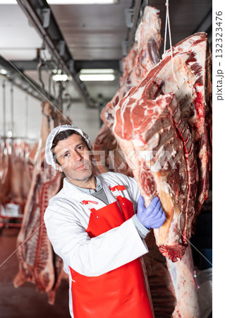 Butcher shop worker hanging slabs of raw beef in cold storage 132323476