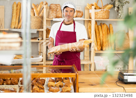 Middle-aged salesman holding paper bag with baguettes in bakery 132323498