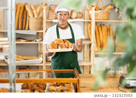 Middle-aged salesman displaying croissants in square wicker basket Middle-aged salesman displaying croissants in square wicker basket 132323503