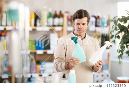 Among shop windows, man buyer leisurely examines goods and chooses glass cleaner spray Among shop windows, man buyer leisurely examines goods and chooses glass cleaner spray 132323530