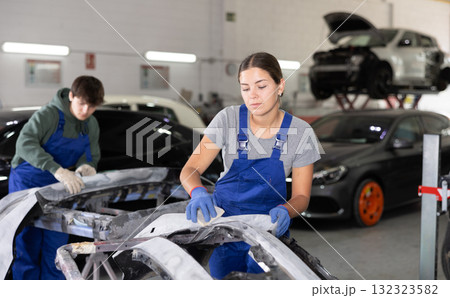 Young female auto mechanic sanding car bumper with sandpaper 132323582