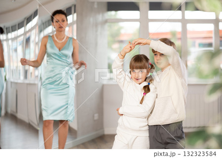 Tween girl and boy practicing waltz in dance hall with female mentor 132323584