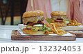 large appetizing burger with meat and vegetables stands on the table next to a garnish of french fries overeating concept. Weight control, overeating calorie counting, junk food addiction 132324053