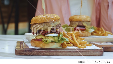 large appetizing burger with meat and vegetables stands on the table next to a garnish of french fries overeating concept. Weight control, overeating calorie counting, junk food addiction large appetizing burger with meat and vegetables stands on the table next to a garnish of french fries overeating concept. Weight control, overeating calorie counting, junk food addiction 132324053